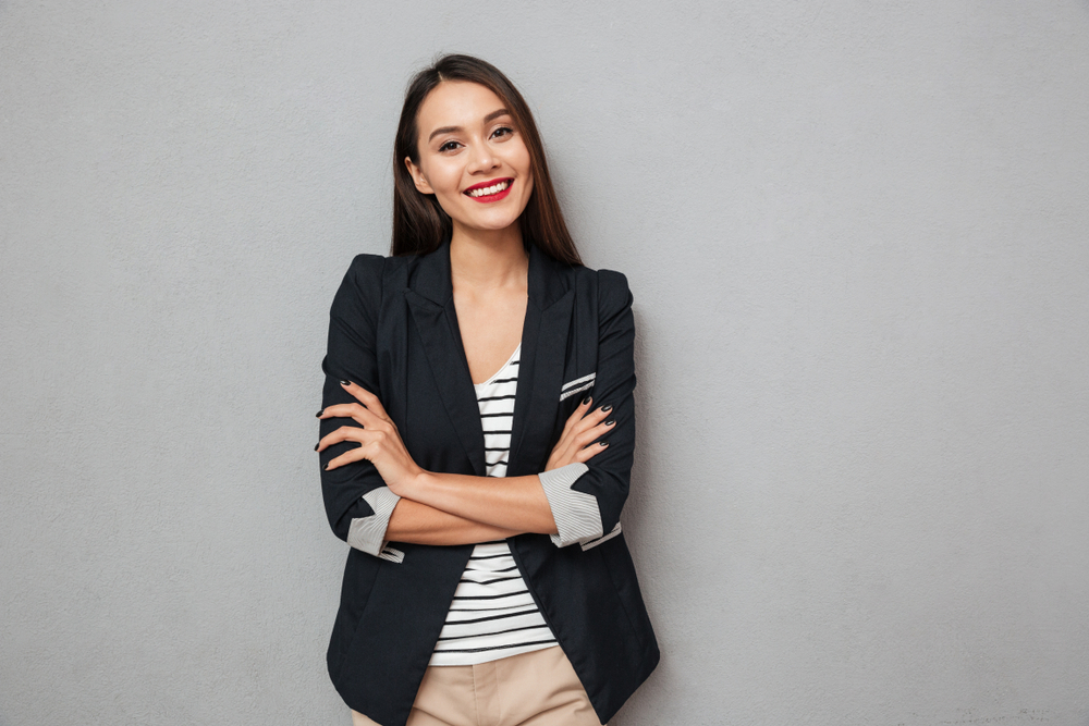 smiling businesswoman in black blazer against grey background